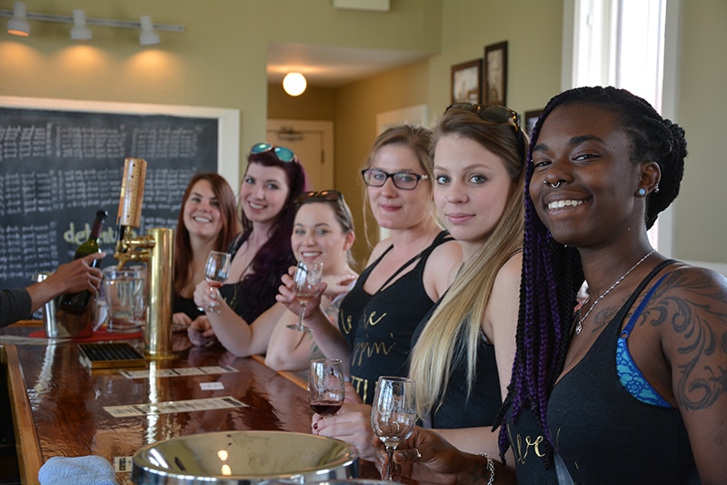 Diverse group of women drinking wine at a winery and smiling at the camera.