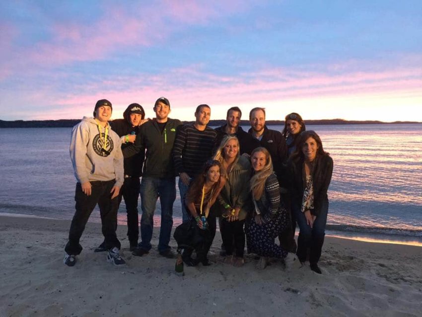 Group of people standing on a beach in front of the water during sunset