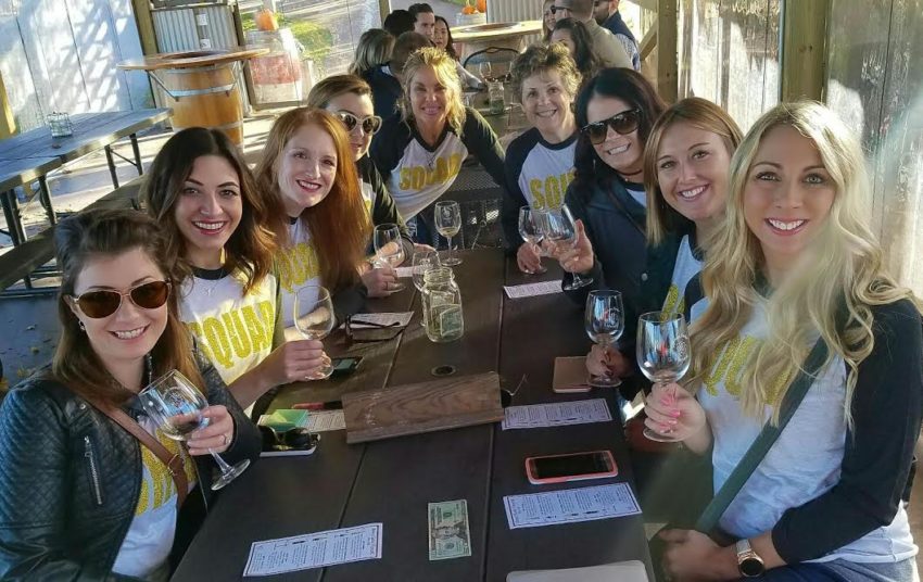 Group of women wearing matching shirts and smilling while tasting wine