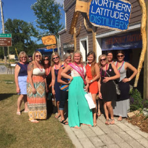 Group of women celebrating a bachelorette party wearing matching necklaces standing in front of a distillery